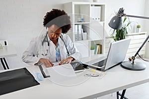 Woman doctor with stethoscope looking at medical papers at her office working hard