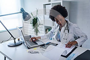 Woman doctor with stethoscope looking at medical papers at her office working hard