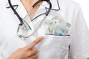 Woman doctor with stethoscope showing polish currency money in apron pocket, corruption or bribe concept