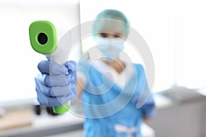 Woman doctor in suit, medical gloves and protective mask measures temperature.