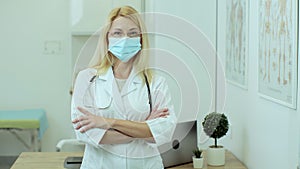 Woman doctor therapist in medical mask standing in office. European woman with glasses professional crossing arms