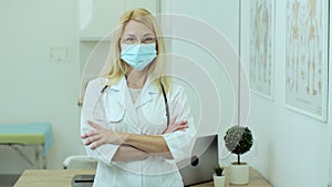 Woman doctor therapist in medical mask standing in office. European woman with glasses professional crossing arms