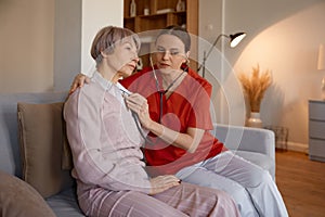 Woman doctor using stethoscope while examining senior woman at nursing home