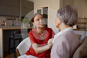 Woman doctor using stethoscope while examining senior woman at nursing home