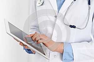 Woman doctor using tablet computer while standing straight in hospital closeup. Healthcare, insurance and medicine