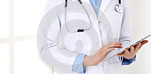 Woman doctor using tablet computer while standing straight in hospital closeup. Healthcare, insurance and medicine