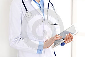 Woman doctor using tablet computer while standing straight in hospital closeup. Healthcare, insurance and medicine