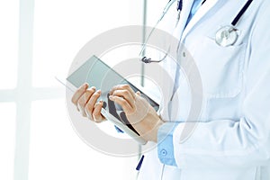 Woman doctor using tablet computer while standing straight in hospital closeup. Healthcare, insurance and medicine