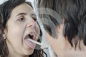 Woman doctor using a tongue depressor with girl patient.