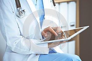 Woman doctor using white tablet computer while sitting at chair in hospital, close-up