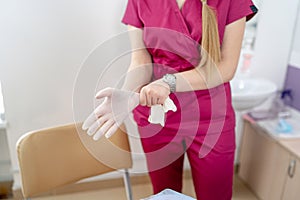 Woman doctor wearing medical sterille gloves. Selective focus on hands. Modern clinic interior in the background.