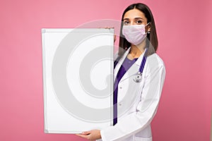 Woman doctor wearing a white medical coat and a mask holding blank board with copy space for text isolated on background