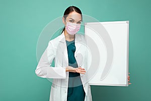 Woman doctor wearing a white medical coat and a mask holding blank board with copy space for text isolated on background