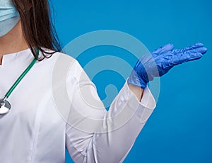 Woman doctor in a white coat, blue latex gloves and a protective mask on his face conditionally holds an object with his hand