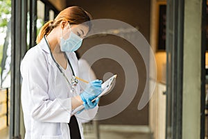 Woman doctor in white coat with stethoscope and blue glove write report by pencil in a notebook at hospital.