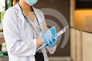 Woman doctor in white coat with stethoscope and blue glove write report by pencil in a notebook in the hospital.