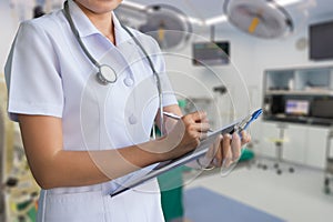 Woman doctor in white coat write report in a notebook on blur background of emergency room, clipping path included