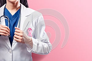 A woman doctor in a white lab coat holding a stethoscope on her hands with pink ribbon over pink background