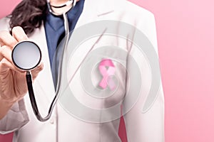 A woman doctor in a white lab coat using with pink ribbon using a stethoscope over pink background