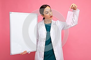Woman doctor in a white medical coat holding blank board with copy space for text and protective mask isolated on