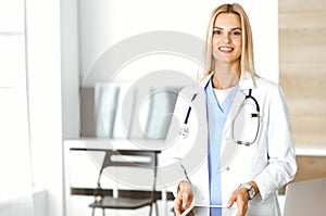 Woman-doctor at work in clinic excited and happy of her profession. Blond female physician is smiling while using tablet