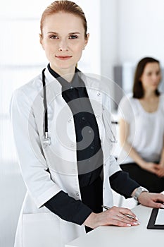 Woman-doctor at work with colleague and patient at background. Middle aged female physician filling up medical documents