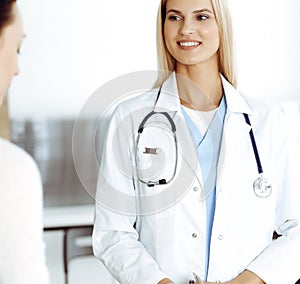 Woman-doctor at work in hospital is happy to consult female patient. Blonde physician checks medical history record and