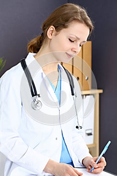 Woman doctor at work at hospital. Young female physician write prescription or filling up medical form while sitting in