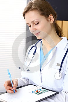 Woman doctor at work at hospital. Young female physician write prescription or filling up medical form while sitting in