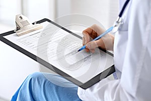 Woman doctor at work at hospital. Young female physician write prescription or filling up medical form while sitting in