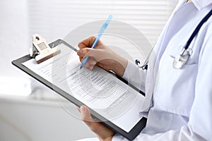 Woman doctor at work at hospital. Young female physician write prescription or filling up medical form while sitting in