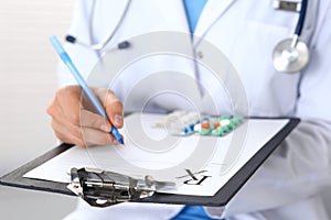 Woman doctor at work at hospital. Young female physician write prescription or filling up medical form while sitting in