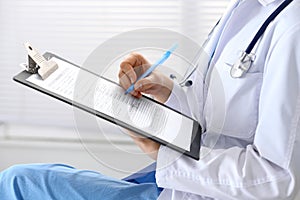 Woman doctor at work at hospital. Young female physician write prescription or filling up medical form while sitting in