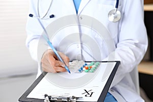 Woman doctor at work at hospital. Young female physician write prescription or filling up medical form while sitting in