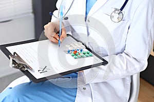 Woman doctor at work at hospital. Young female physician write prescription or filling up medical form while sitting in