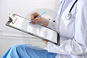 Woman doctor at work at hospital. Young female physician write prescription or filling up medical form while sitting in