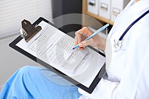 Woman doctor at work at hospital. Young female physician write prescription or filling up medical form while sitting in