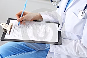 Woman doctor at work at hospital. Young female physician write prescription or filling up medical form while sitting in