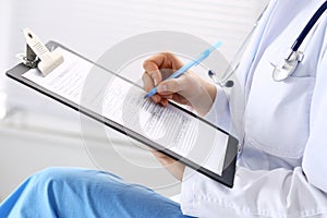 Woman doctor at work at hospital. Young female physician write prescription or filling up medical form while sitting in