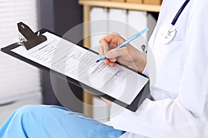 Woman doctor at work at hospital. Young female physician write prescription or filling up medical form while sitting in