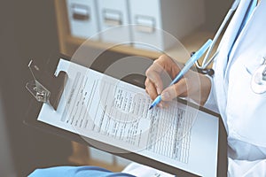 Woman doctor at work at hospital. Young female physician write prescription or filling up medical form while sitting in