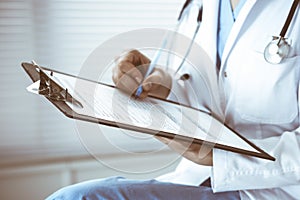 Woman doctor at work at hospital. Young female physician write prescription or filling up medical form while sitting in