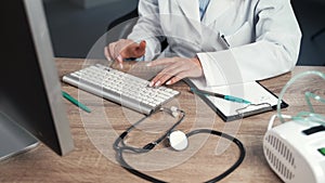 Woman doctor working at computer, entering data from patient file.