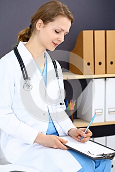 Woman doctor write prescription or filling up medical form while sitting in hospital office