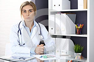 Woman doctor write prescription while sitting in hospital office. A lot of various colored pills liye at her clipboard