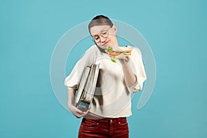 Woman with documents is talking on the phone and is about to eat a sandwich