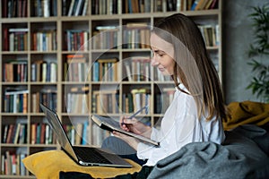 Woman with documents using a laptop at home against the background of a rack of books