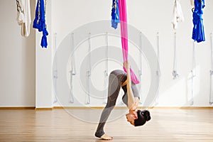 Woman does aerial yoga exercises, leans with straight legs.