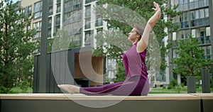 Woman does bends forward to her feet on the bench in the yard of an apartment building, fitness in the urban environment