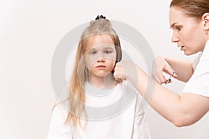 A woman does haircut a funny girl's on a white background.